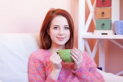 Redhead girl with cup sitting on a sofa at home
